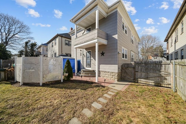 rear view of property featuring a balcony, a gate, a fenced backyard, and a yard