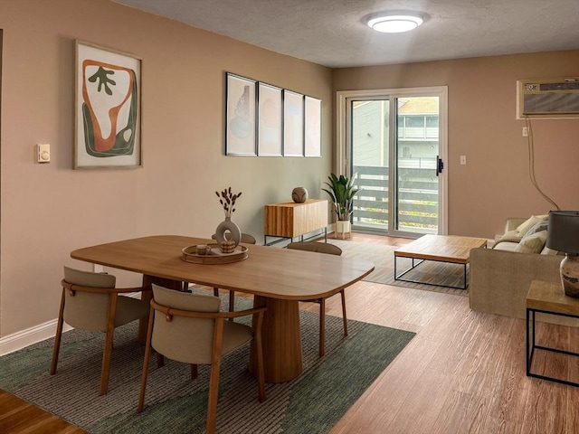 dining room with a wall mounted air conditioner, light wood-style flooring, a textured ceiling, and baseboards