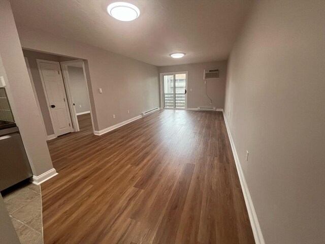 empty room with baseboard heating, a wall unit AC, wood finished floors, and baseboards
