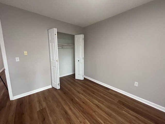 unfurnished bedroom featuring baseboards, dark wood-type flooring, and a closet