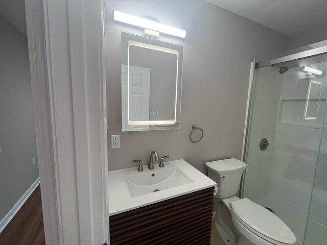 bathroom featuring a stall shower, toilet, vanity, and wood finished floors