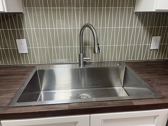 kitchen view of butcher block counters, a sink, and white cabinetry