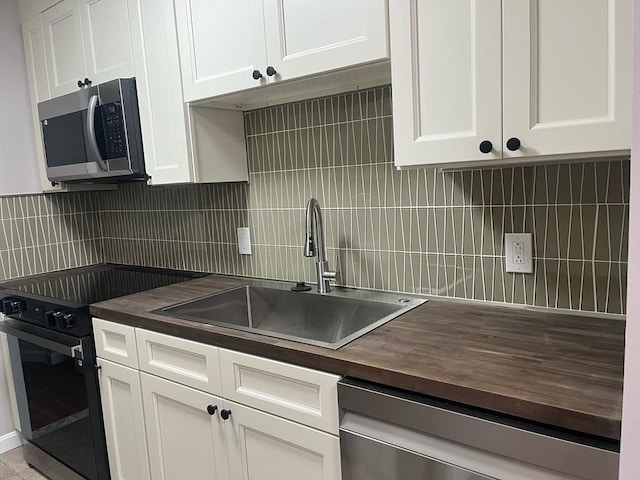 kitchen with stainless steel appliances, wooden counters, a sink, and backsplash