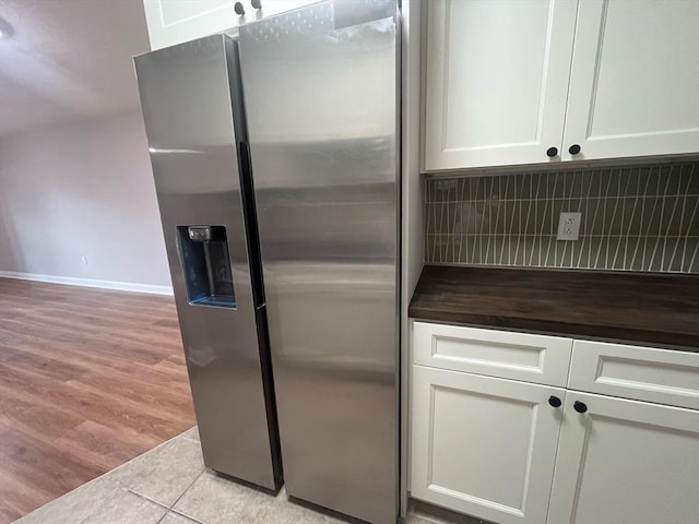 kitchen featuring stainless steel fridge with ice dispenser, backsplash, wood counters, white cabinetry, and light tile patterned floors