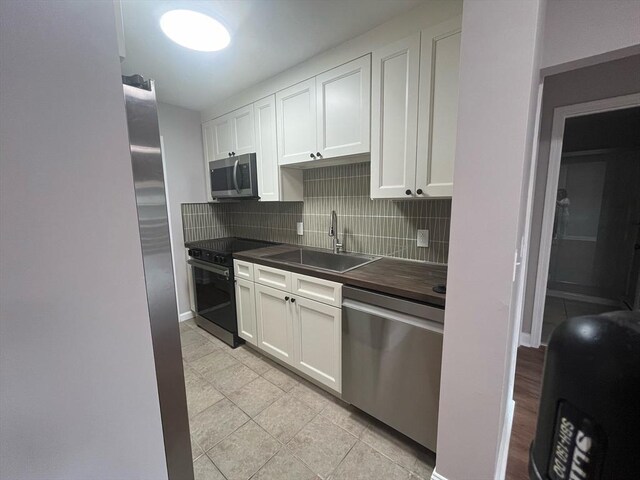 kitchen featuring appliances with stainless steel finishes, a sink, backsplash, white cabinets, and butcher block counters