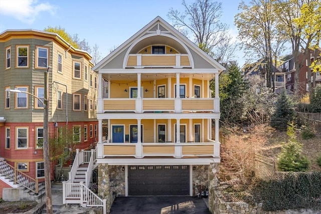 view of front facade featuring stairs, aphalt driveway, a garage, a porch, and a balcony
