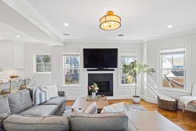 living area featuring visible vents, light wood finished floors, crown molding, and a wealth of natural light
