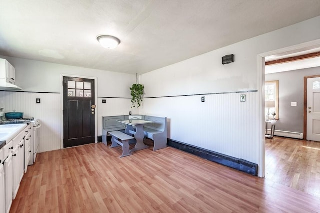 dining room with a baseboard radiator, light wood finished floors, and wainscoting