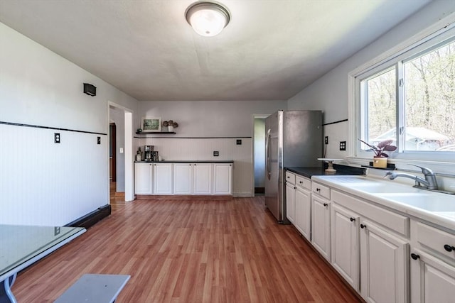 kitchen with freestanding refrigerator, white cabinets, a sink, and light wood-style flooring