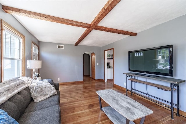 living area featuring beam ceiling, arched walkways, baseboards, wood finished floors, and visible vents