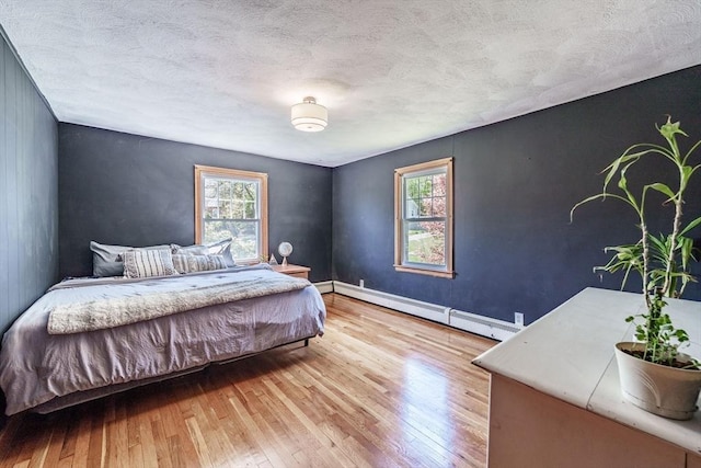 bedroom featuring baseboards, a textured ceiling, a baseboard heating unit, and wood finished floors