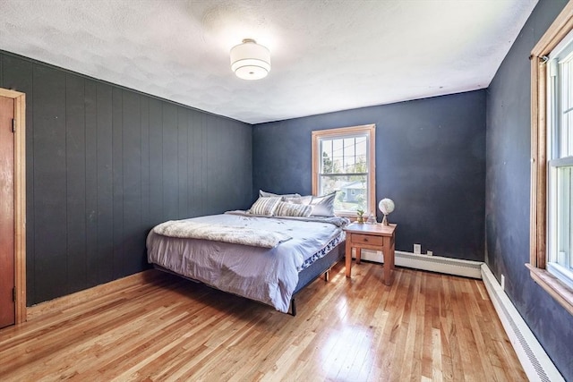 bedroom featuring wood walls, baseboard heating, and light wood-type flooring
