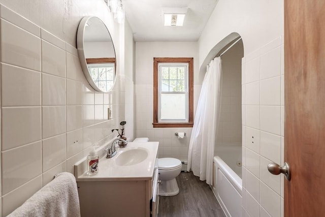 full bath with shower / bath combination with curtain, tile walls, wood finished floors, vanity, and toilet