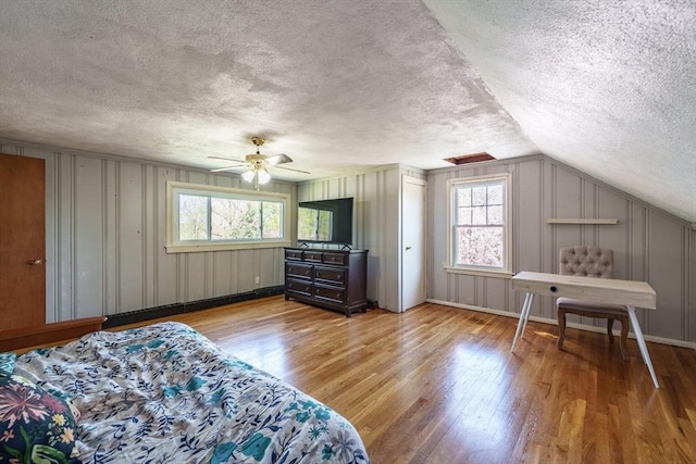 bedroom with a textured ceiling, multiple windows, and light wood-style floors