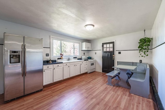 kitchen with gas range gas stove, light wood-type flooring, a sink, stainless steel fridge, and white cabinetry
