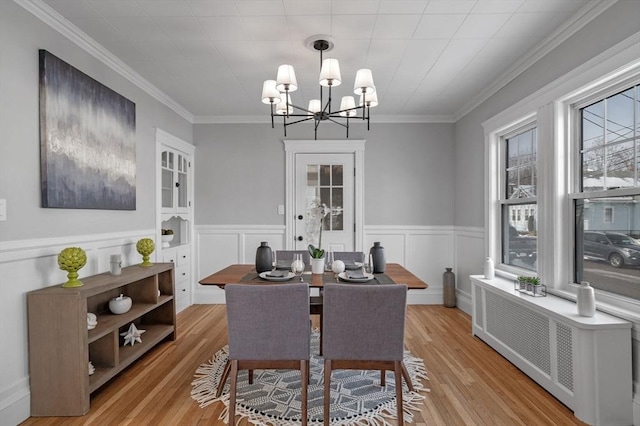 dining space with crown molding, radiator, light hardwood / wood-style floors, and a notable chandelier