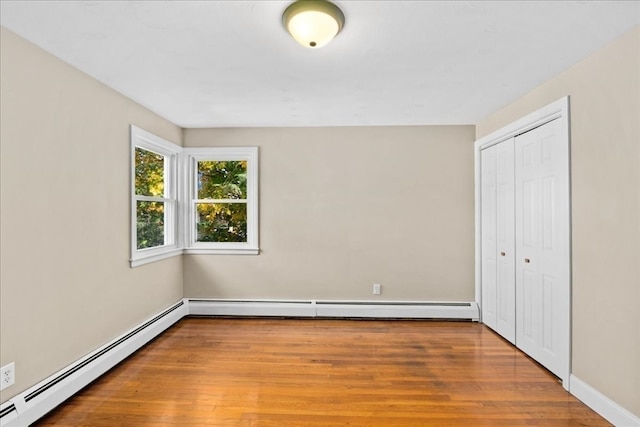 unfurnished bedroom with a closet, wood-type flooring, and a baseboard heating unit