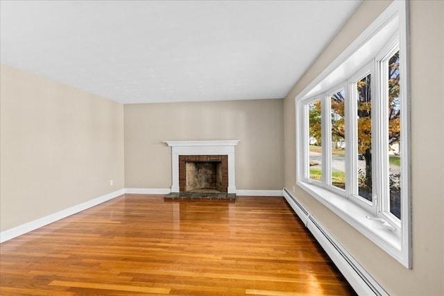 unfurnished living room with baseboard heating, light hardwood / wood-style floors, and a brick fireplace