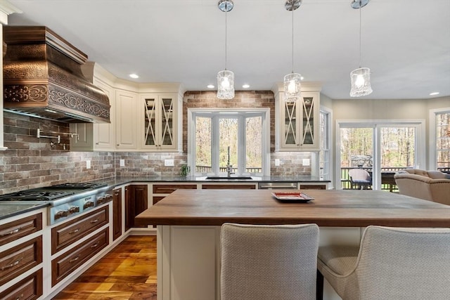 kitchen featuring appliances with stainless steel finishes, a sink, wood counters, decorative backsplash, and custom range hood