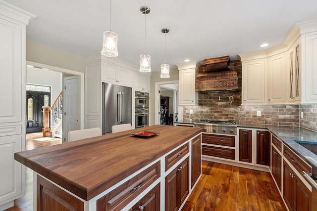 kitchen with butcher block countertops, custom range hood, dark wood-style floors, and stainless steel appliances