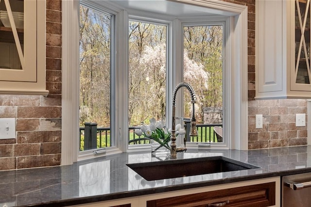 interior details with decorative backsplash, a sink, dark stone countertops, glass insert cabinets, and white cabinetry
