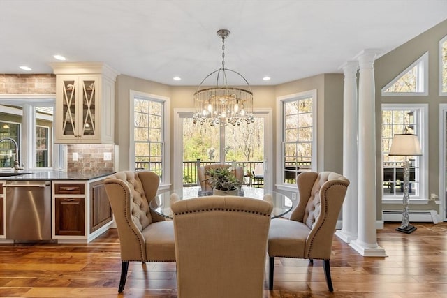 dining area featuring ornate columns, a notable chandelier, a healthy amount of sunlight, and hardwood / wood-style floors