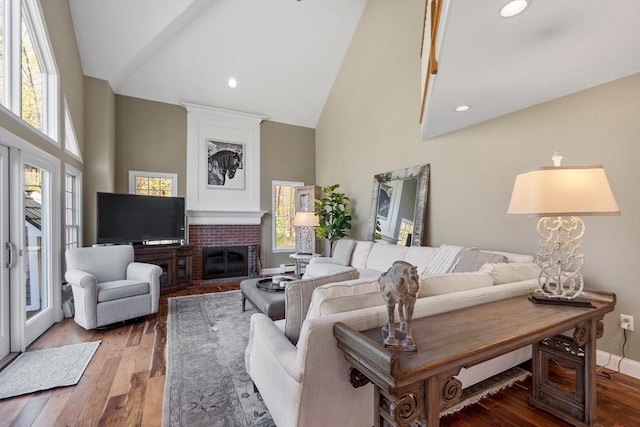 living room with a fireplace, wood finished floors, high vaulted ceiling, baseboards, and recessed lighting