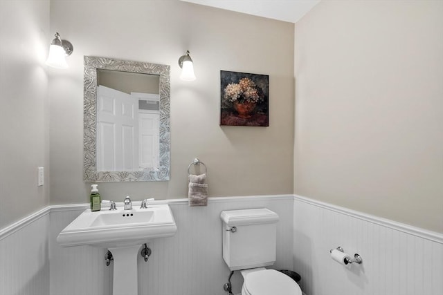 half bathroom featuring toilet, wainscoting, and a sink