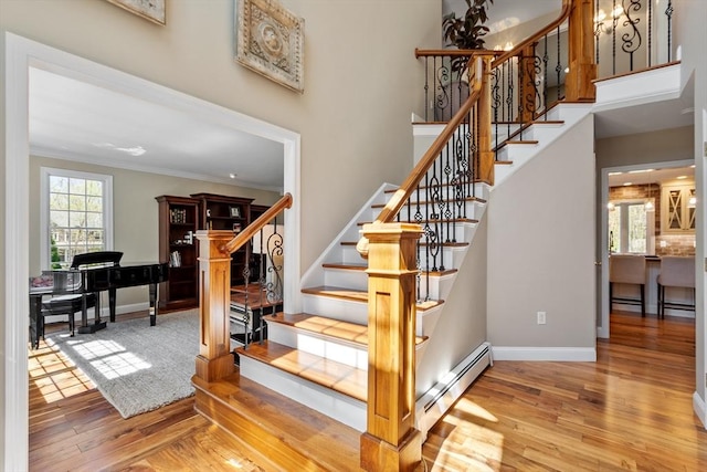stairway with crown molding, baseboards, a baseboard heating unit, and wood finished floors