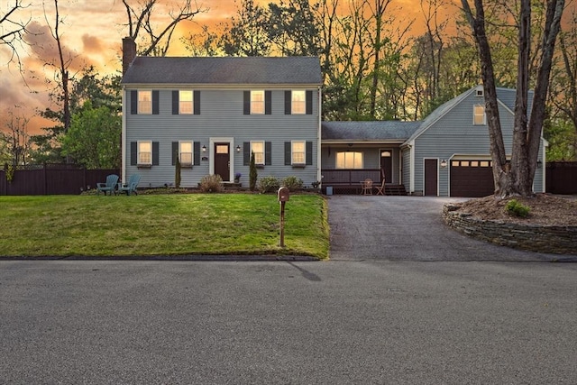 colonial inspired home with a garage, a front lawn, aphalt driveway, fence, and a chimney