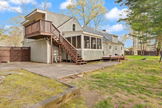 back of property featuring a wooden deck, a patio, a sunroom, a gate, and a lawn