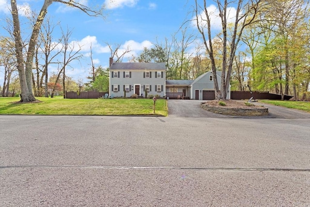 colonial house with driveway, a chimney, fence, a front lawn, and an attached garage
