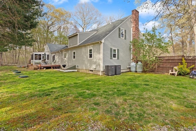 back of property with a chimney, a lawn, a wooden deck, a sunroom, and fence