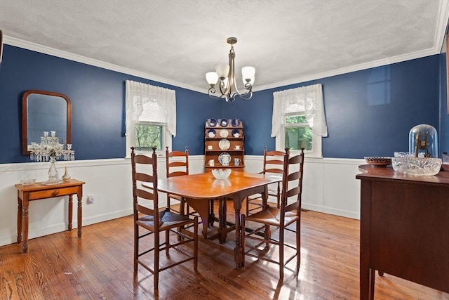 dining area with ornamental molding, wainscoting, wood finished floors, and a chandelier
