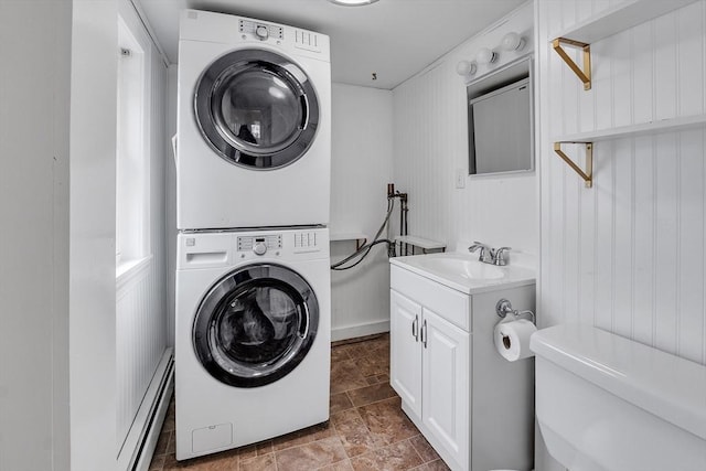 laundry area with stacked washer / dryer, a baseboard radiator, a sink, and stone finish flooring