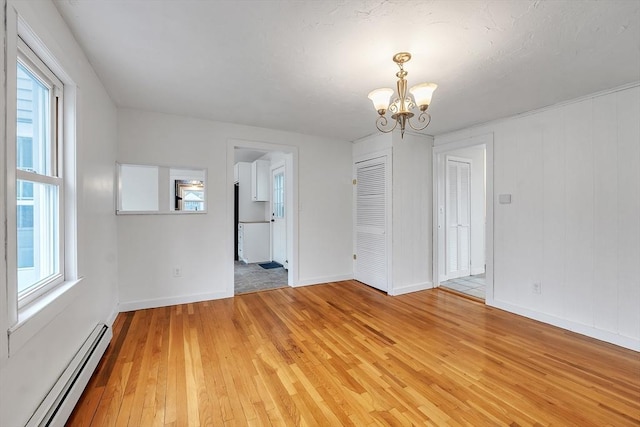 unfurnished dining area with baseboard heating, a chandelier, light wood-type flooring, and baseboards