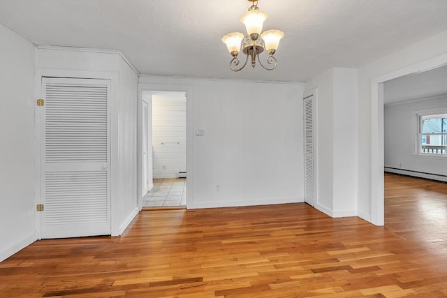 unfurnished dining area featuring a baseboard radiator, a chandelier, light wood finished floors, baseboard heating, and baseboards
