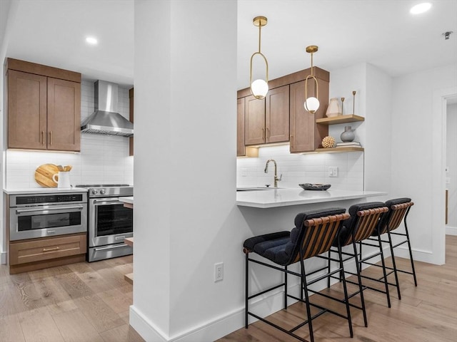 kitchen with pendant lighting, wall chimney exhaust hood, decorative backsplash, a kitchen bar, and stainless steel appliances