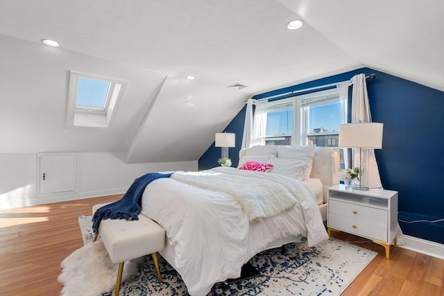 bedroom featuring multiple windows, lofted ceiling with skylight, and light hardwood / wood-style floors