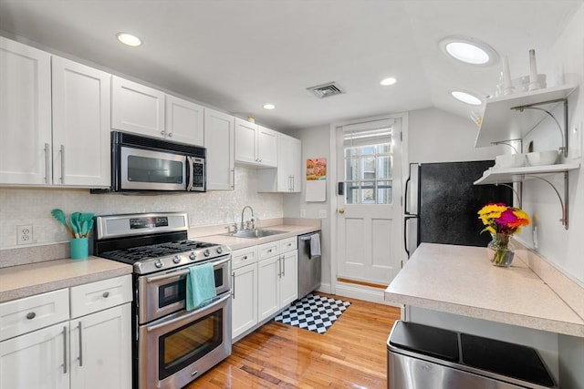 kitchen featuring sink, light wood-type flooring, appliances with stainless steel finishes, white cabinets, and backsplash