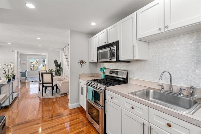 kitchen with sink, white cabinetry, appliances with stainless steel finishes, light hardwood / wood-style floors, and backsplash