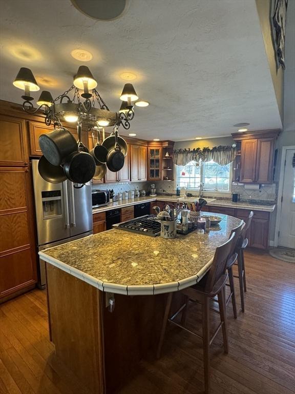 kitchen with stainless steel appliances, light countertops, a center island, brown cabinetry, and glass insert cabinets