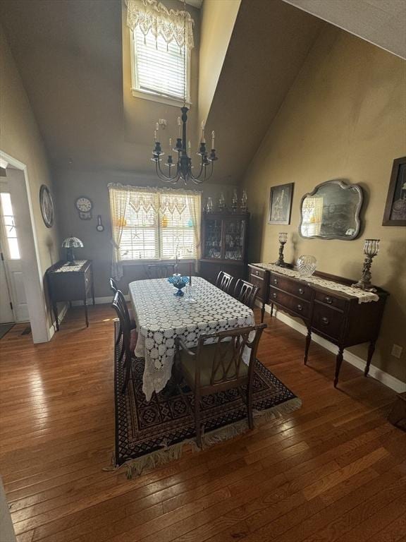 dining space featuring a chandelier, a wealth of natural light, high vaulted ceiling, and wood finished floors