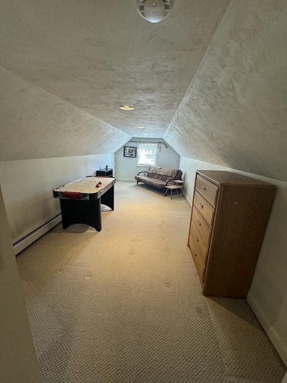 additional living space with a baseboard heating unit, vaulted ceiling, a textured ceiling, and light colored carpet