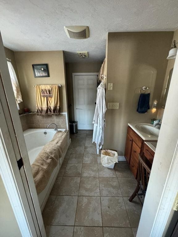 full bathroom featuring a textured ceiling, a garden tub, vanity, and tile patterned floors