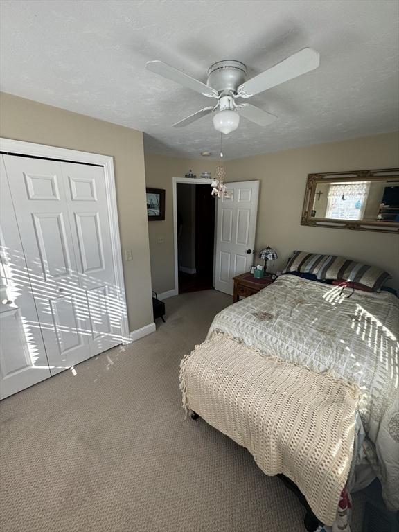 carpeted bedroom featuring a textured ceiling, a closet, a ceiling fan, and baseboards