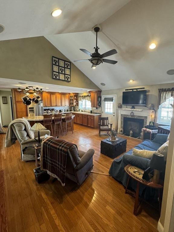 living room with ceiling fan, high vaulted ceiling, wood finished floors, and a glass covered fireplace