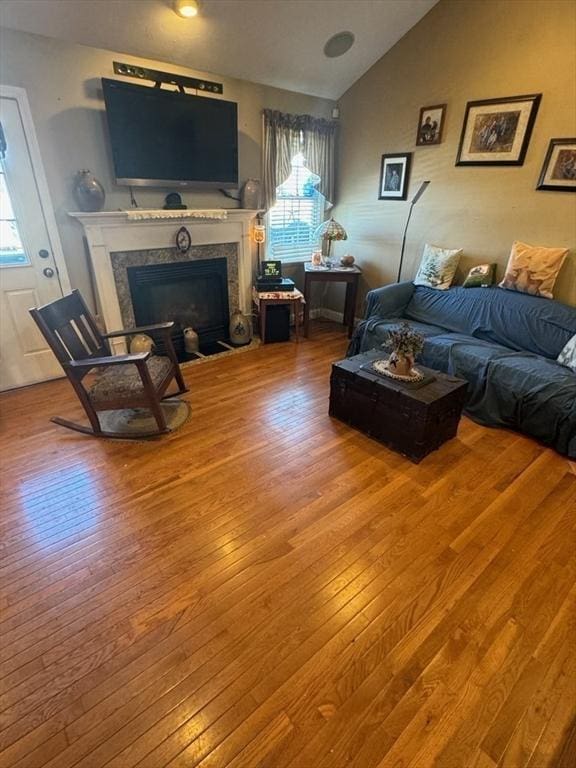 living area featuring a glass covered fireplace, vaulted ceiling, and wood finished floors