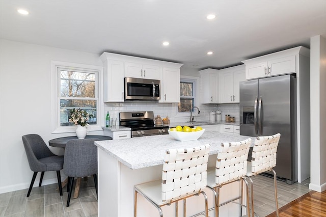 kitchen featuring white cabinetry, light stone countertops, stainless steel appliances, a kitchen breakfast bar, and a kitchen island