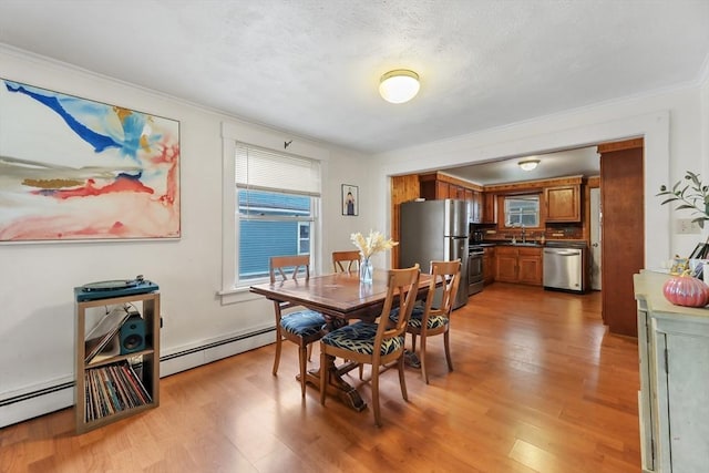 dining room featuring sink, ornamental molding, light hardwood / wood-style floors, and baseboard heating